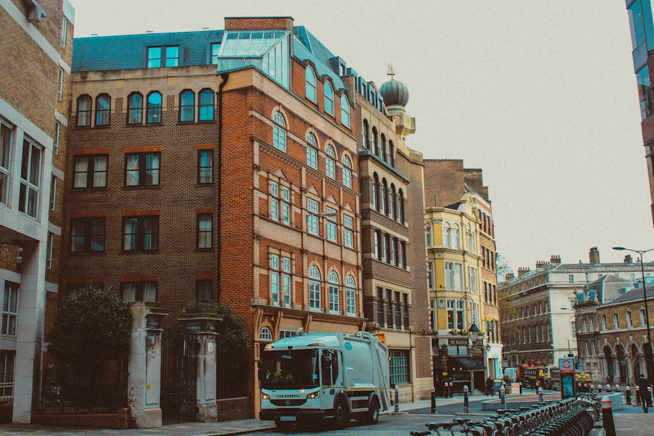 A street scene in Battersea featuring a light blue van operated by Man and Van Battersea, parked on the pavement in front of a row of multi-storey buildings with various architectural styles, includin